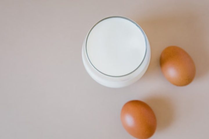 Aesthetic flatlay featuring a glass of milk and two brown eggs on a light surface.